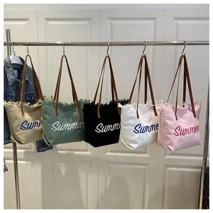 Primer plano de cinco bolsos tote de lona con bordado Summer y bordes deshilachados