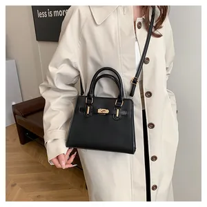 Detail of minimalist black leather trapezoid handbag with gold hardware and shoulder strap