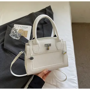 Detail of white litchi pattern leather handbag with metal lock on a minimalist bed
