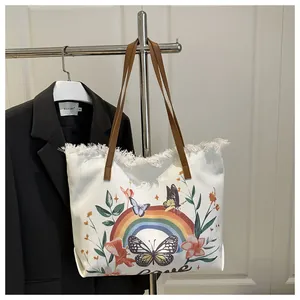 Détail du cabas en toile avec broderie colorée, pompons et poignées en cuir marron