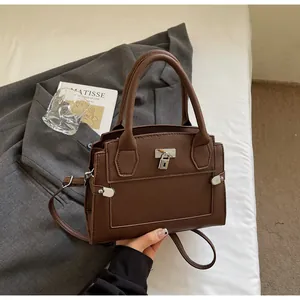 Detail of dark brown lychee leather handbag with classic silver lock on a white bed