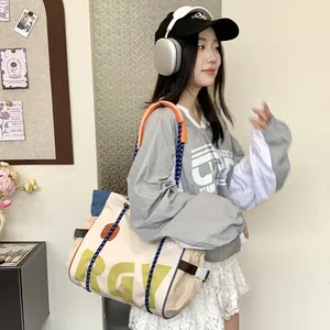 Close-up of beige canvas tote bag with orange handle and blue denim side stitching