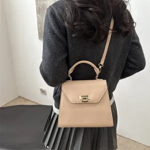 Elegante borsa a trapezio beige con chiusura dorata indossata da modella in un interno
