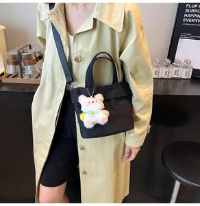 Black tote bag with a pink teddy bear charm shown on a trench coat model