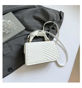 Detail van witte gewatteerde crossbodytas met V-stiksels en gouden metalen gespen
