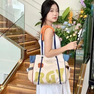 Detail of canvas tote bag showing yellow letter print and orange rope handle attachment