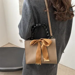 Elegant khaki square bridal handbag with silk bow and black woven handle shown on shoulder