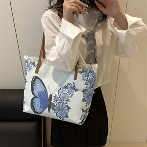 Sac fourre-tout bleu avec broderie papillon et franges blanches porté à l'épaule