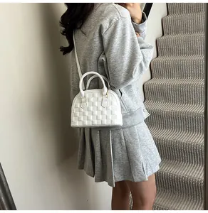 Detail view of white shell bag with quilted texture and gold-tone hardware strap