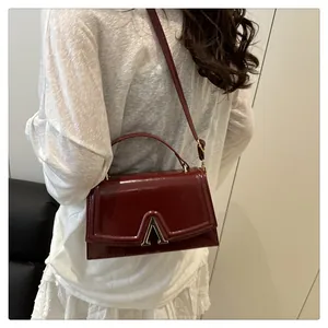 Détail du sac à main en cuir verni rouge foncé avec boucle en métal doré en forme de V