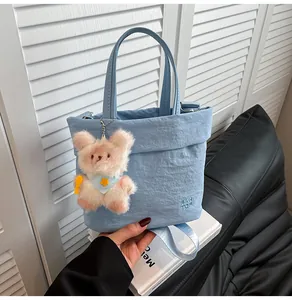 Detail of light blue nylon tote bag showing wrinkled texture and plush bear charm