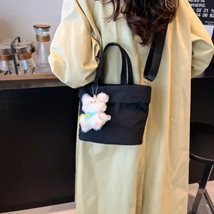 Chic black high-capacity tote bag with plush bear charm on a stylish trench coat model