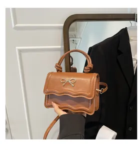 Close-up of brown synthetic leather crossbody bag with golden bow and scalloped edges
