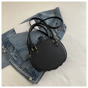 Detail of a matte black pumpkin-shaped crossbody bag with gold hardware on denim