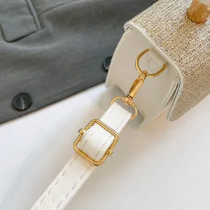 Detail of adjustable white leather shoulder strap and shiny golden glitter flap on bag