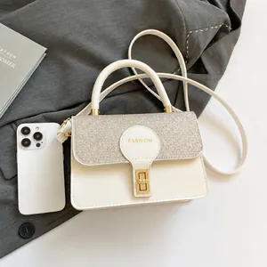 Detail view of cream shoulder bag with gold shimmer flap and size reference to a phone