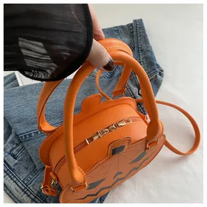 Close-up of bright orange pumpkin crossbody bag with jack-o'-lantern face on denim pants