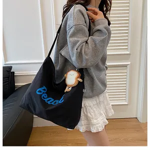 Detail of a black canvas tote bag featuring blue Beach embroidery and a plush toast charm