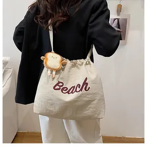 Detail of off-white canvas tote bag with purple Beach text and cute toast plush charm