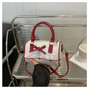 Detail of white cylinder bag with red bow, ruffle edges, and heart charm on a bench