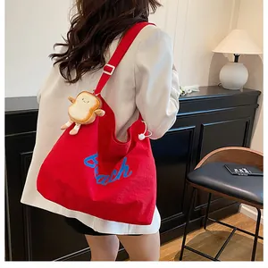 Close-up of red canvas tote bag featuring a plush toast charm and adjustable white strap