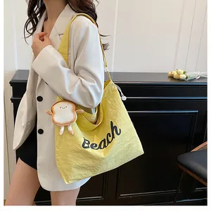 Detail of yellow canvas tote bag with black Beach lettering and plush toast charm
