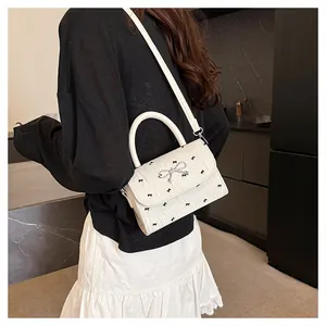 Détail du sac à main blanc crème avec imprimé nœud, texture plissée et boucle argentée