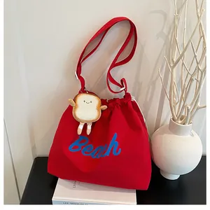 Detail of red canvas tote bag with Beach lettering, drawstring and plush toast charm