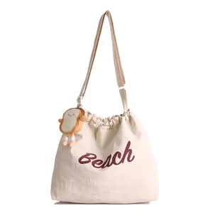 Off-white canvas tote bag with burgundy Beach print and a cute plush bread charm