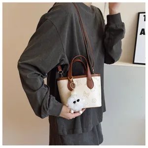 Detail of contrast color bucket bag with cartoon prints and plush ball charm accessory