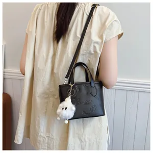 Detail of black embossed crossbody bag with butterfly patterns and a plush charm