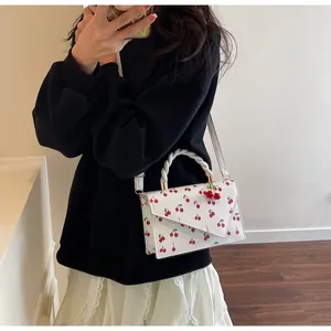Detail of white cherry print handbag featuring a braided handle and 3D cherry charm