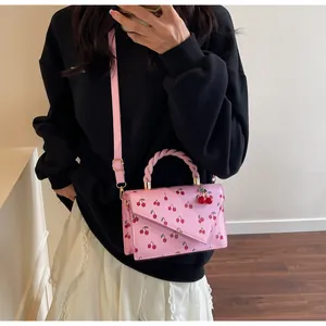 Detail view of pink cherry print handbag featuring twisted handle and cherry charm ornament