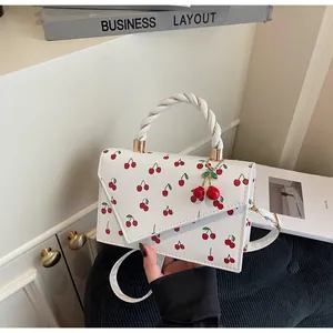 Close-up of a white rectangular bag with red cherry prints and 3D cherry charm detail