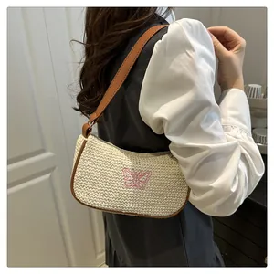 Detail der geflochtenen Strohtasche mit rosa Schmetterlingsstickerei und braunem Lederbesatz