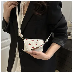 Close-up van de mini crème crossbodytas met kersenprint en goudkleurige bies op model