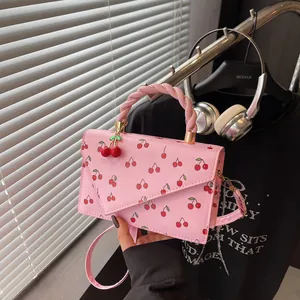 Pink cherry print crossbody bag with woven handle and cherry charm in lifestyle setting