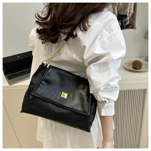 Detail of black square shoulder bag with snakeskin texture and golden metal buckle
