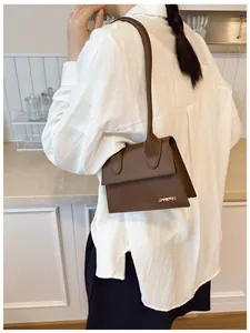 Modella che indossa una borsa a tracolla marrone scuro con logo dorato in una cucina moderna