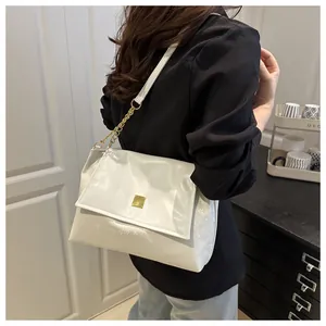 Detail view of white textured shoulder bag with golden lock and chain on a model
