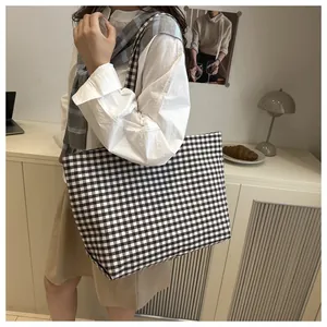 Detail of a large brown gingham canvas tote bag worn over the shoulder in a casual setting