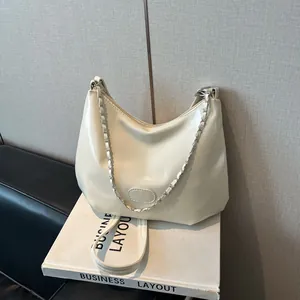 Détail d'un sac hobo beige crème avec chaîne argentée sur un livre blanc