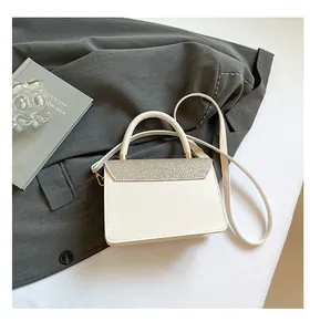 Detalle de bolso bandolera crema con solapa de purpurina plateada y herrajes metálicos