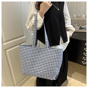 Blue and white gingham canvas tote bag worn by a model in a cozy indoor setting
