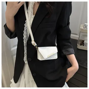 Detail van witte mini crossbodytas met asymmetrische flap en gouden metalen accentbalk