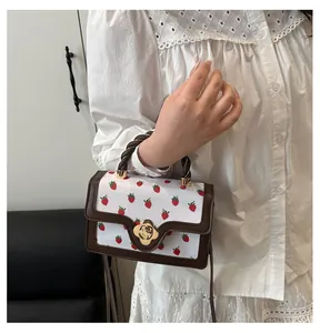 Detail of strawberry print crossbody bag featuring floral gold lock and twisted top handle