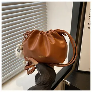 Detalle de bolso saco de piel plisada caramelo con cordón y colgante de cordero
