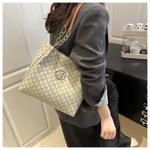 Détail d'un sac bandoulière en cuir avec imprimé M et chaîne porté par un mannequin