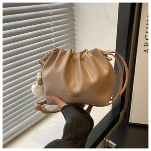 Detalle de bolso cubo plisado albaricoque con logotipo dorado y colgante de peluche