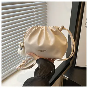 Detalle de bolso tipo cubo plisado blanco roto con letras doradas y colgante suave